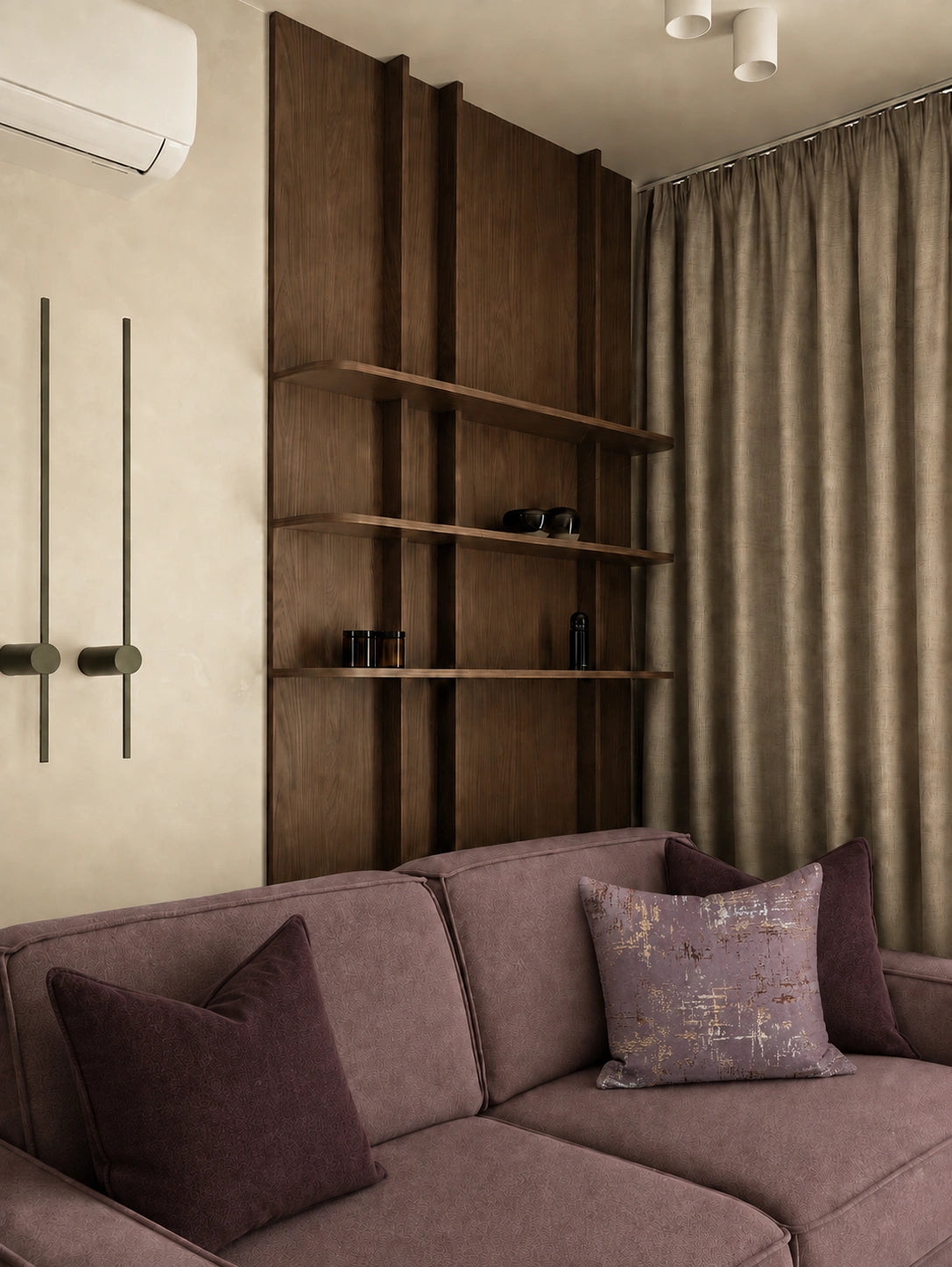 A modern living room corner featuring a mauve-purple fabric sofa with dark purple and patterned accent pillows, set against a beige wall with a tall dark wood shelving unit and textured taupe curtains.