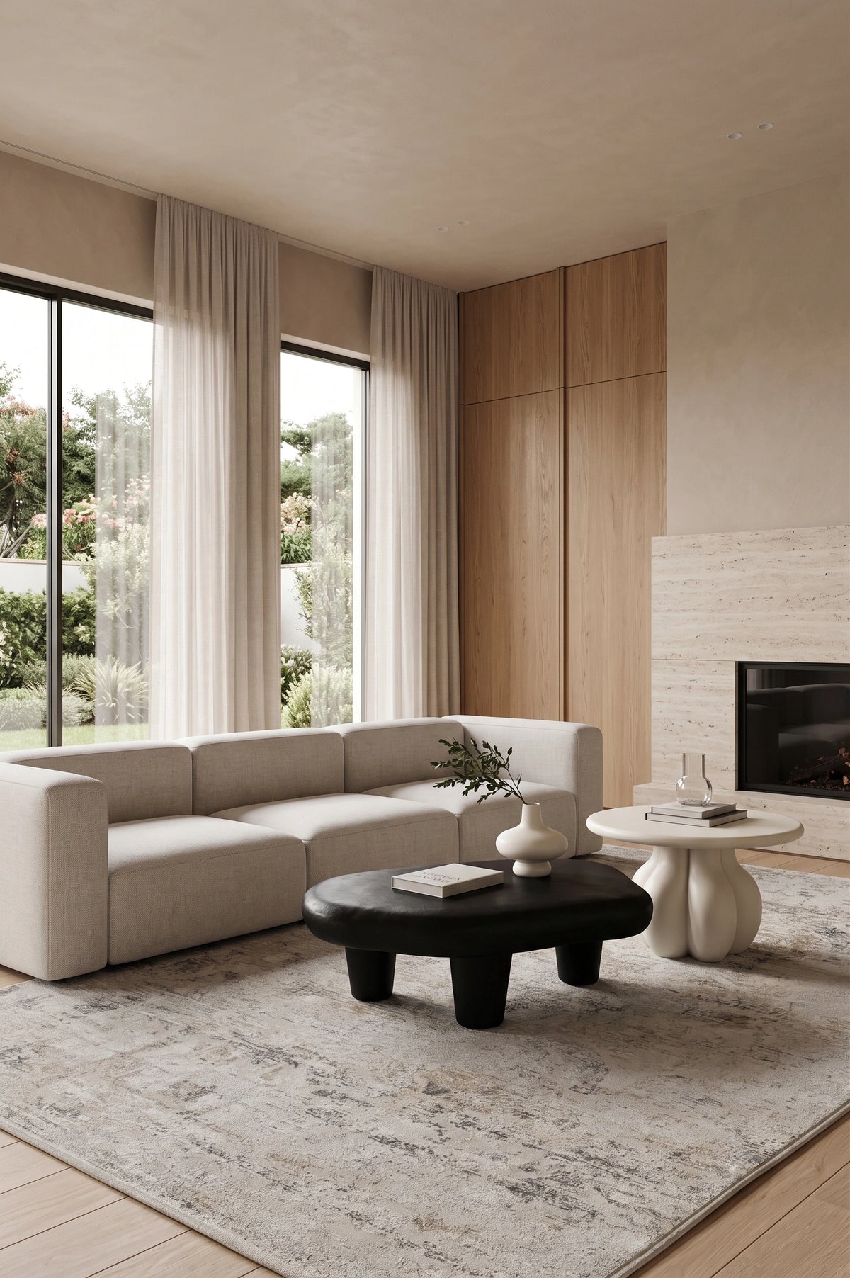 A modern living room featuring a light beige sectional sofa, a round black coffee table, a textured gray area rug, and a fireplace with light wood paneling.