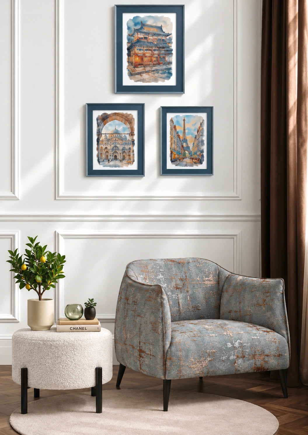Three framed watercolor art prints with blue frames hang on a white paneled wall above a gray upholstered armchair and a small white side table with a plant.