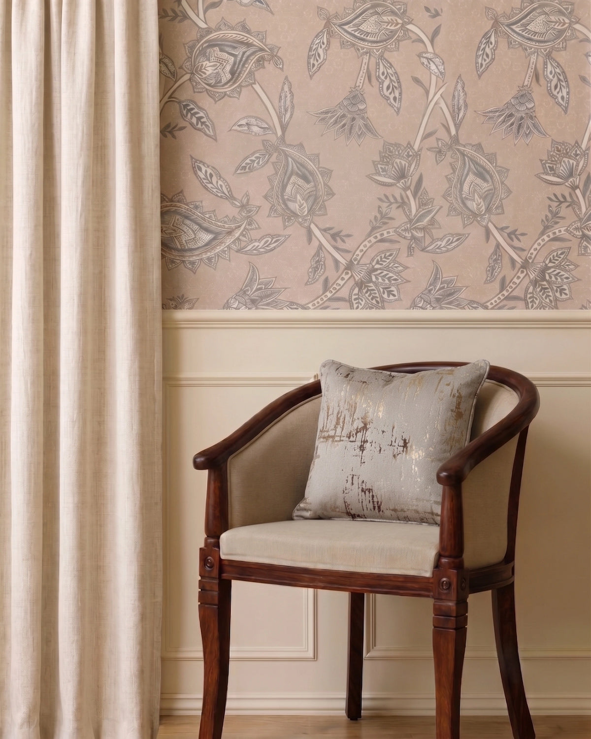 A styled interior corner showing a wooden armchair with a beige cushion and pillow, set against a wall with beige floral wallpaper and a cream curtain.