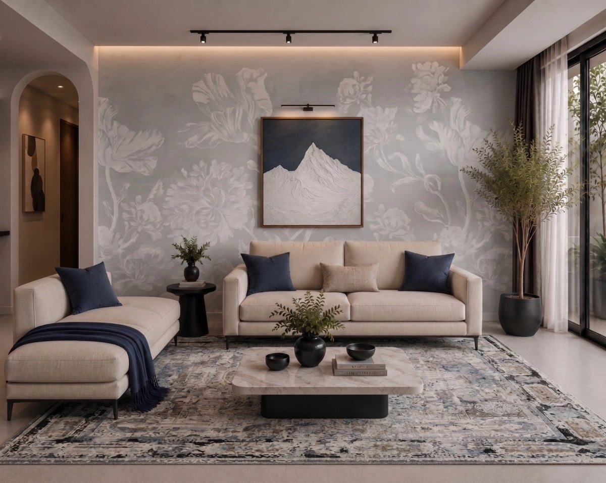 A modern living room featuring a beige sofa and chaise lounge with navy blue pillows and a throw blanket, set on a large patterned area rug. A matching rectangular coffee table sits in front.