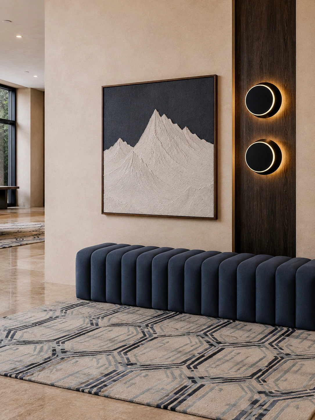 A modern interior scene featuring a large framed art print of a mountain on a dark background, mounted on a beige wall above a dark blue ribbed bench and a patterned rug.