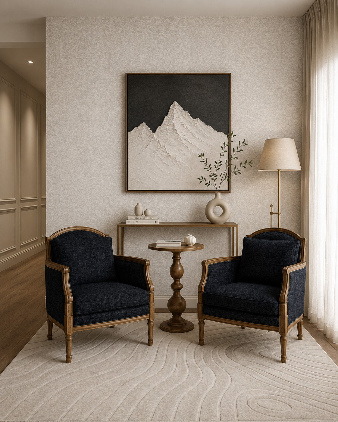 A styled interior scene with two dark blue upholstered armchairs facing a small round wooden side table, set in a living room with a beige textured wall, a framed mountain artwork, a floor lamp, and a patterned rug.