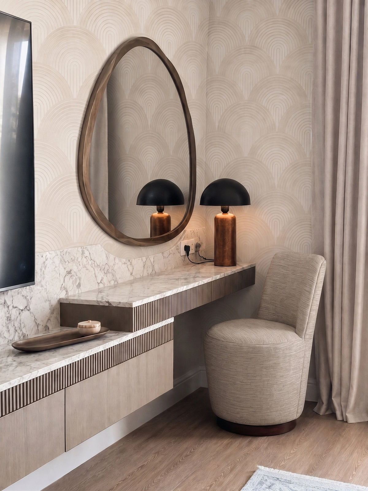 Contemporary bedroom workspace featuring a marble-topped floating console, oversized oval mirror, textured geometric wallpaper, twin black and wood table lamps, upholstered accent chair, wood flooring, and neutral curtains.
