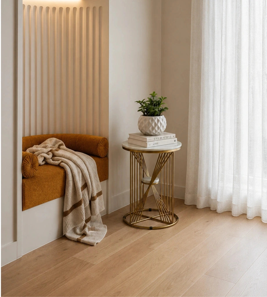 Nook with a brown cushioned bench, gold side table with books and plant, and white curtains.