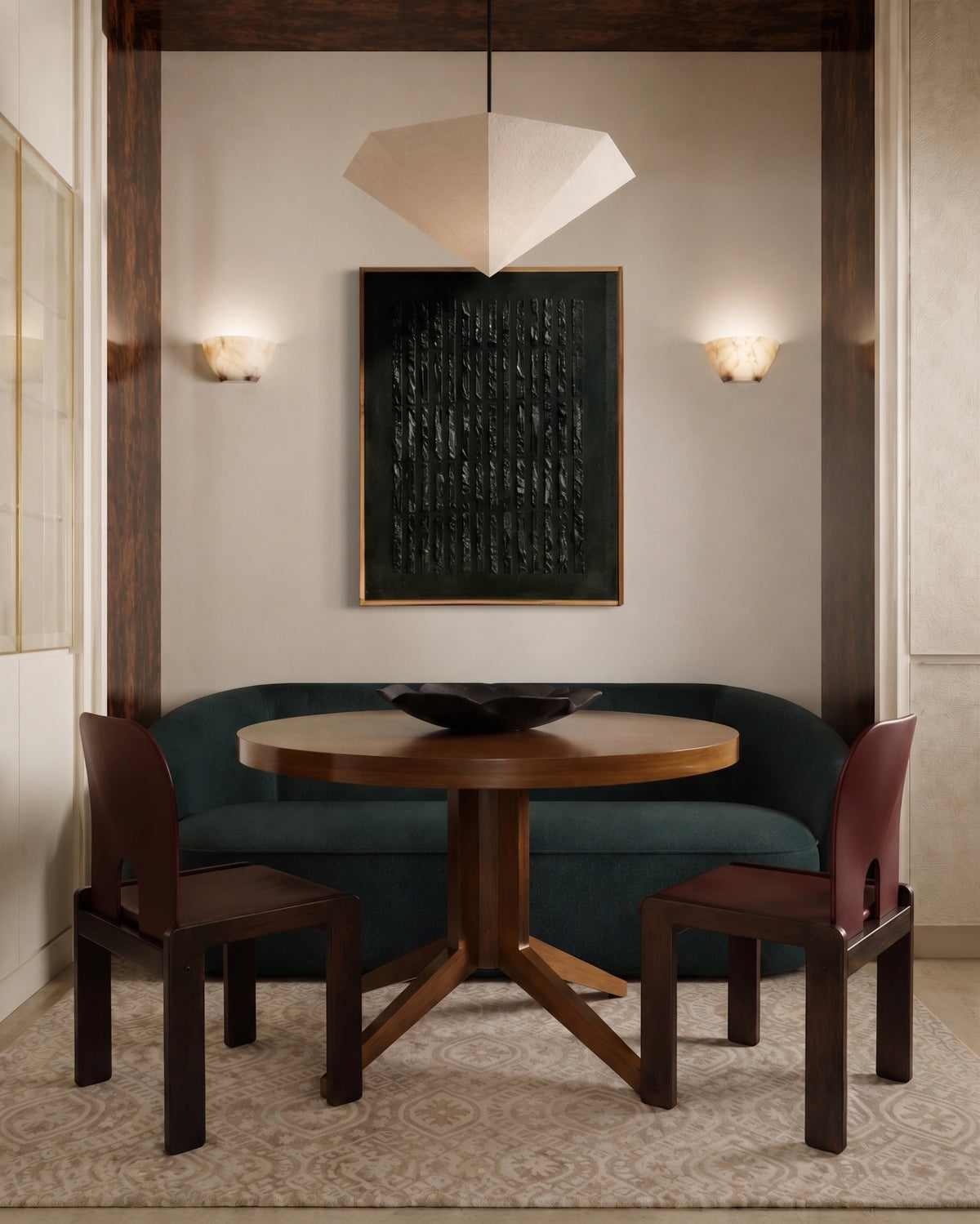 A styled interior dining nook featuring a round wooden table, two dark wood chairs with burgundy seats, a curved teal upholstered bench, and a large dark framed wall art piece above.