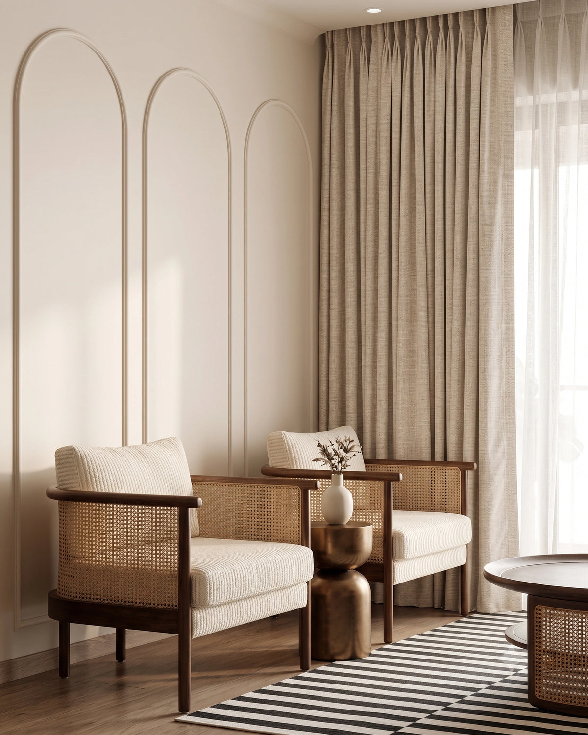 A styled interior room with two wooden armchairs featuring woven cane seats and cream cushions, positioned beside floor-length beige curtains and a striped rug.